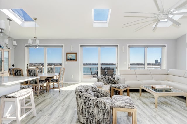 living room featuring lofted ceiling with skylight, light wood-style flooring, an inviting chandelier, and a water view