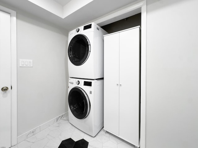 washroom with baseboards, cabinet space, stacked washer and dryer, and marble finish floor