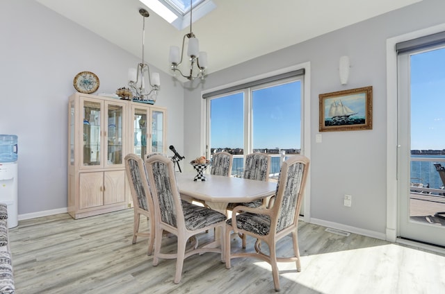 dining area featuring lofted ceiling with skylight, a notable chandelier, baseboards, and light wood finished floors