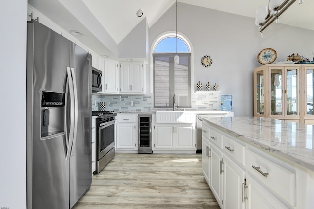 kitchen featuring a sink, white cabinetry, wine cooler, appliances with stainless steel finishes, and light stone countertops