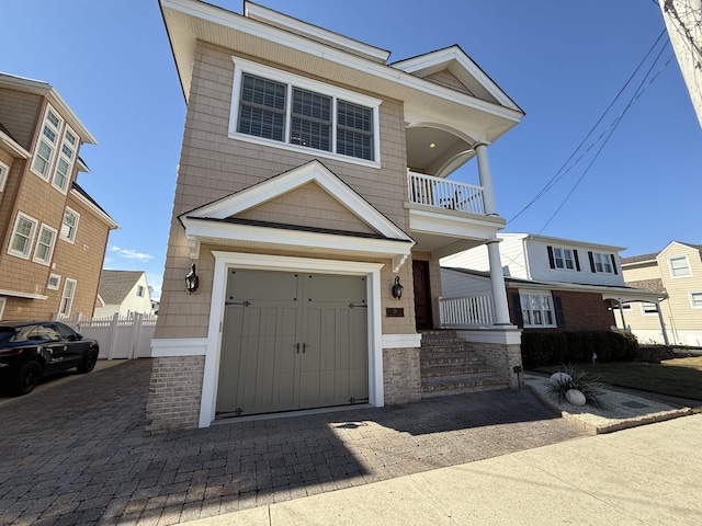 view of front facade featuring decorative driveway, a balcony, a garage, and fence