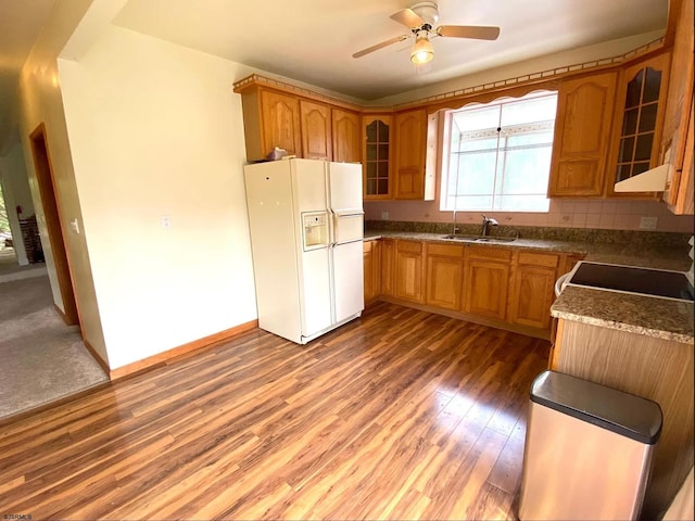 kitchen featuring wood finished floors, a sink, white refrigerator with ice dispenser, glass insert cabinets, and brown cabinets