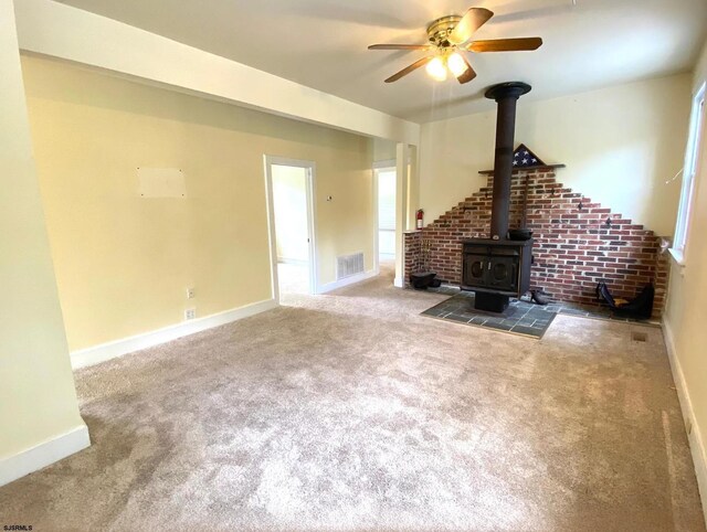 unfurnished living room with a ceiling fan, carpet, visible vents, baseboards, and a wood stove