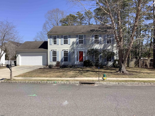 colonial home with an attached garage, concrete driveway, and fence