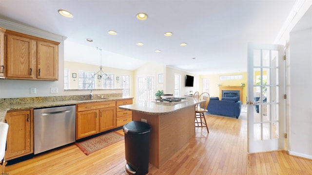 kitchen featuring light wood finished floors, a kitchen bar, a fireplace, stainless steel dishwasher, and a sink