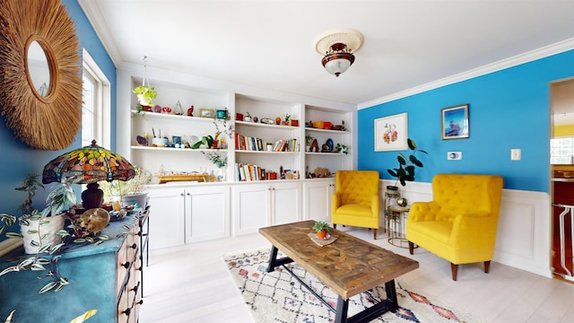 sitting room with light wood-type flooring, a wainscoted wall, built in shelves, and ornamental molding