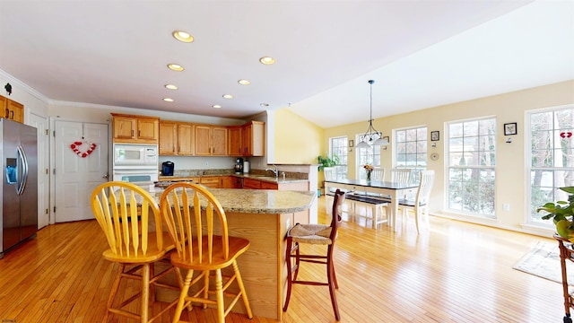 kitchen with white appliances, a breakfast bar area, light stone countertops, a sink, and light wood-style floors