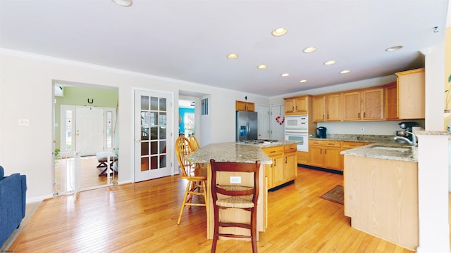 kitchen with light wood-style flooring, appliances with stainless steel finishes, ornamental molding, and a sink