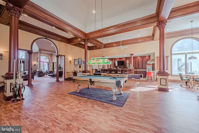 rec room with a high ceiling, wood finished floors, crown molding, and ornate columns