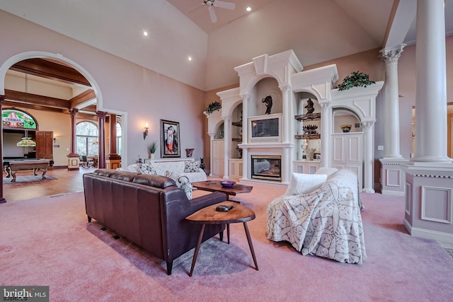 carpeted living room with arched walkways, high vaulted ceiling, a ceiling fan, and ornate columns