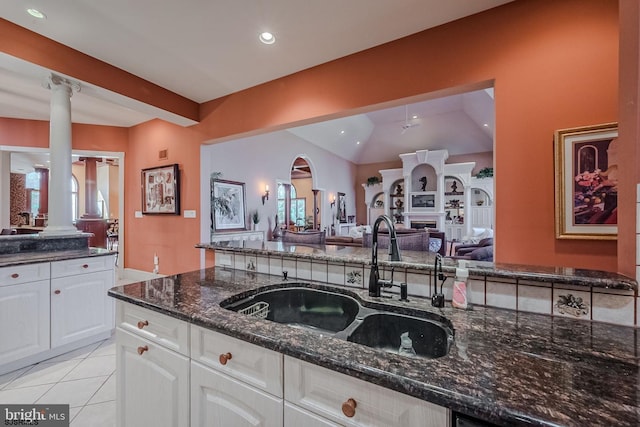 kitchen featuring dark stone countertops, light tile patterned floors, ornate columns, a sink, and open floor plan