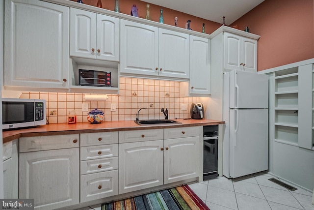 kitchen featuring stainless steel microwave, visible vents, freestanding refrigerator, white cabinets, and a sink