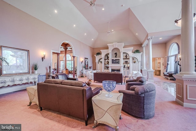 living room featuring ceiling fan, light colored carpet, a fireplace, high vaulted ceiling, and ornate columns