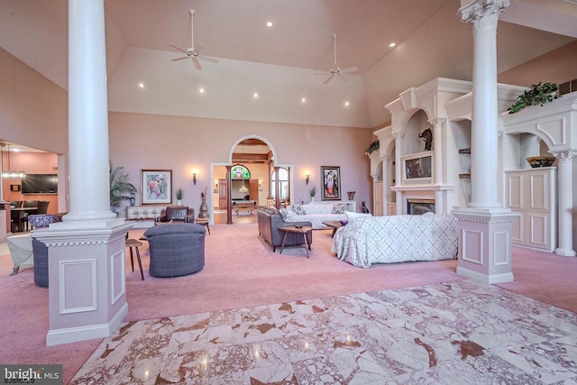 living area with decorative columns, carpet, ceiling fan, and high vaulted ceiling