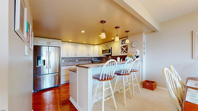 kitchen featuring a breakfast bar, a peninsula, decorative backsplash, appliances with stainless steel finishes, and pendant lighting