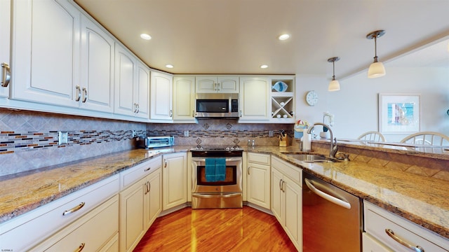 kitchen featuring backsplash, light wood-type flooring, appliances with stainless steel finishes, hanging light fixtures, and a sink