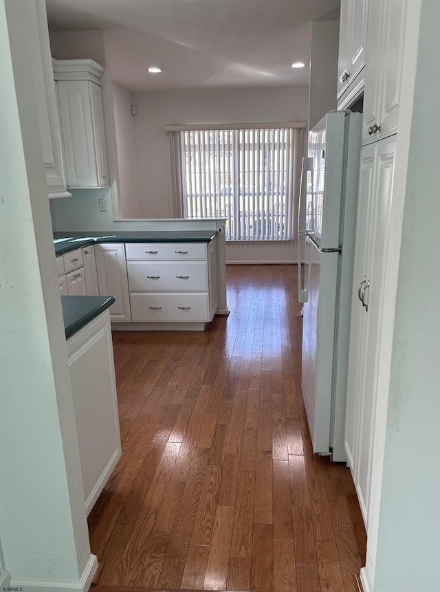 kitchen with a peninsula, freestanding refrigerator, hardwood / wood-style flooring, white cabinets, and dark countertops