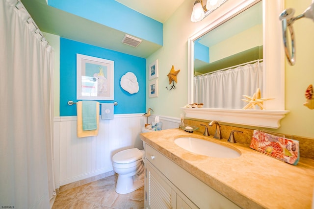 bathroom featuring a wainscoted wall, visible vents, toilet, tile patterned flooring, and vanity