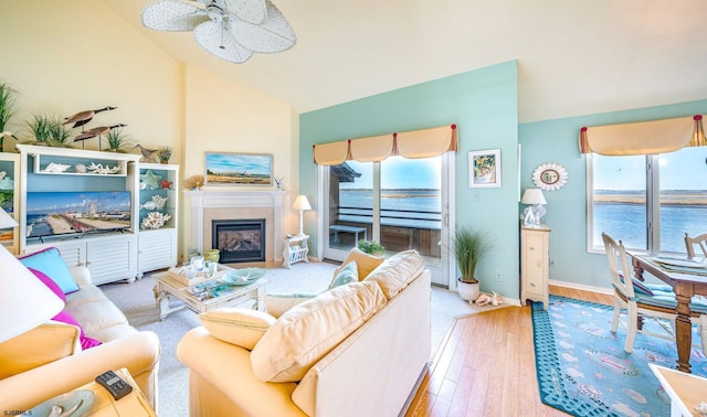 living room with a water view, a glass covered fireplace, wood finished floors, baseboards, and ceiling fan