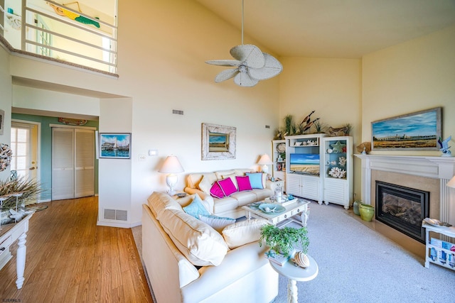 living room with high vaulted ceiling, visible vents, wood finished floors, and a glass covered fireplace