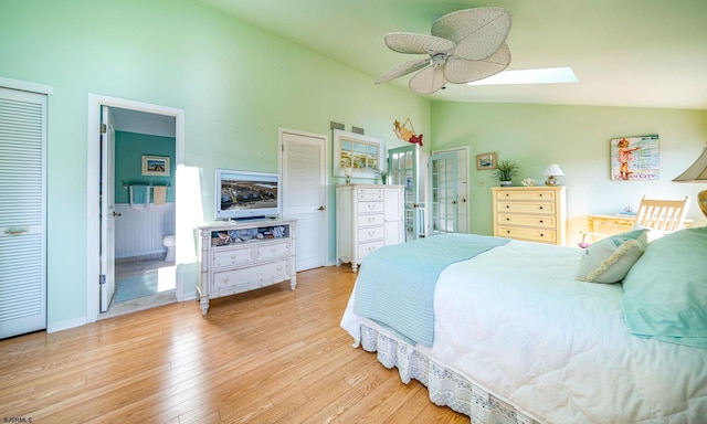 bedroom featuring vaulted ceiling with skylight, two closets, light wood-style flooring, and connected bathroom