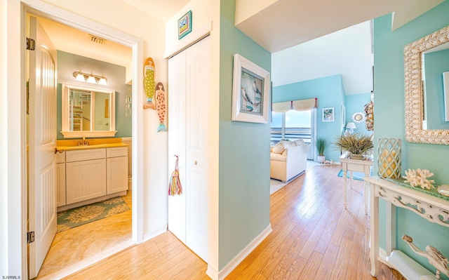 hallway with baseboards, visible vents, light wood-type flooring, and a sink