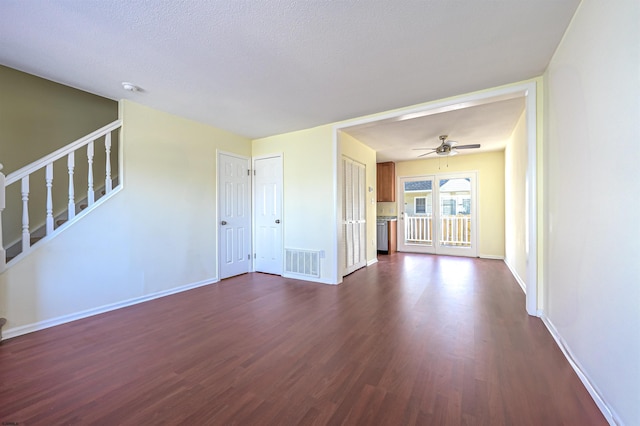 unfurnished living room featuring dark wood-style floors, baseboards, visible vents, a ceiling fan, and stairs