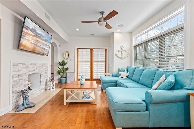 living area featuring a stone fireplace, arched walkways, a wealth of natural light, and light wood-type flooring