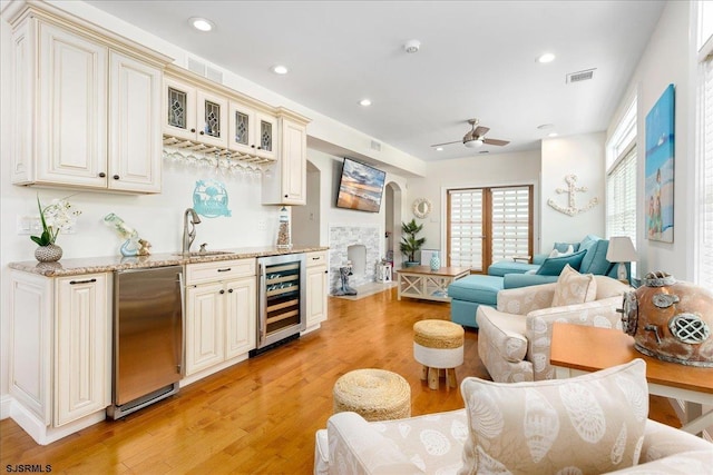 interior space featuring cream cabinetry, wine cooler, light wood-style flooring, stainless steel refrigerator, and a sink