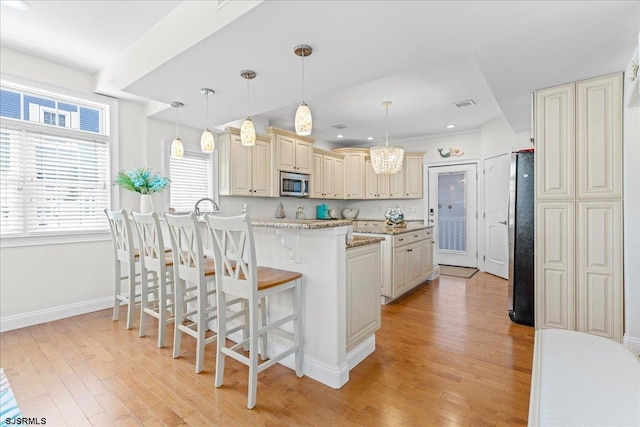 kitchen featuring a kitchen bar, light wood-type flooring, appliances with stainless steel finishes, a peninsula, and cream cabinetry