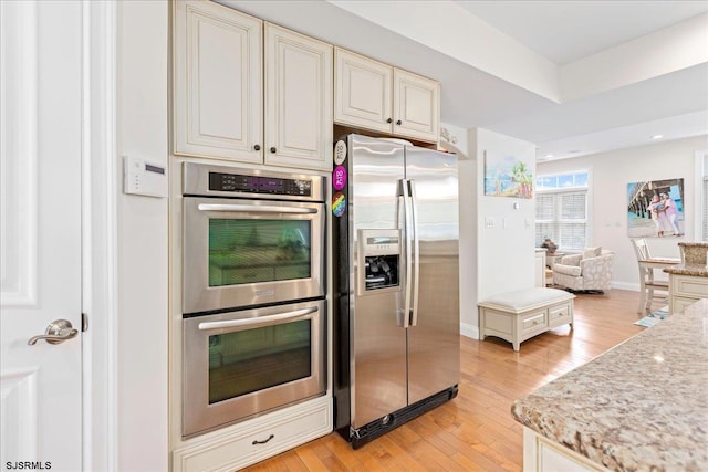 kitchen featuring light wood finished floors, baseboards, light stone counters, recessed lighting, and appliances with stainless steel finishes