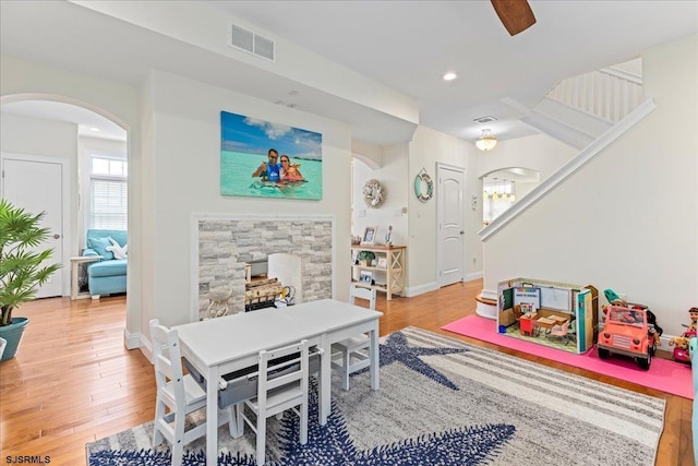 recreation room with a stone fireplace, arched walkways, visible vents, and light wood finished floors