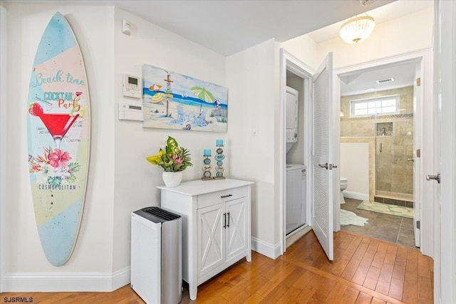 hallway featuring stacked washing maching and dryer, light wood-type flooring, and baseboards