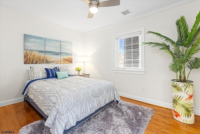 bedroom with ceiling fan, visible vents, baseboards, and wood finished floors