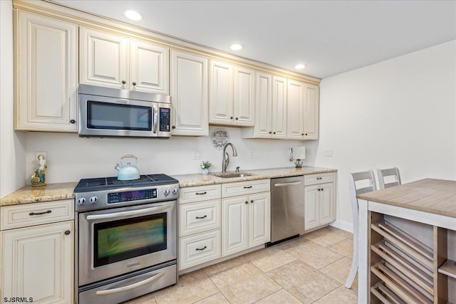 kitchen with light stone countertops, appliances with stainless steel finishes, cream cabinets, and a sink