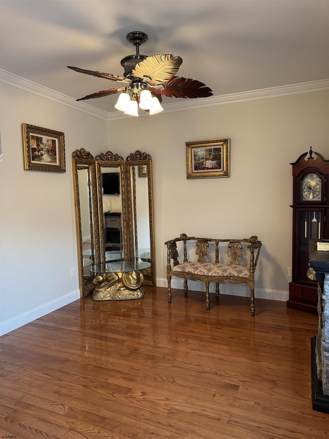 sitting room with a ceiling fan, wood finished floors, baseboards, a fireplace, and crown molding