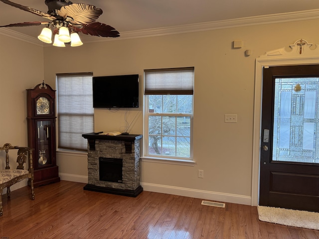 foyer featuring visible vents, ornamental molding, wood finished floors, a stone fireplace, and ceiling fan