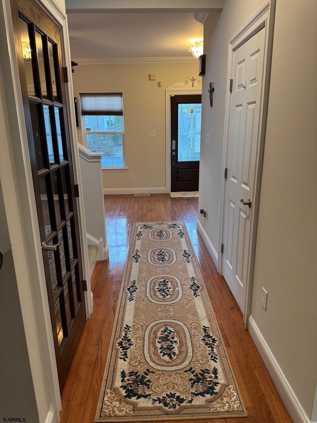 hallway with baseboards, wood-type flooring, and ornamental molding