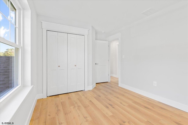 unfurnished bedroom with visible vents, baseboards, light wood-type flooring, and a closet