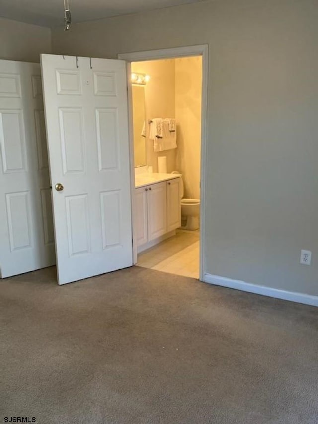 unfurnished bedroom featuring baseboards, light colored carpet, and ensuite bath