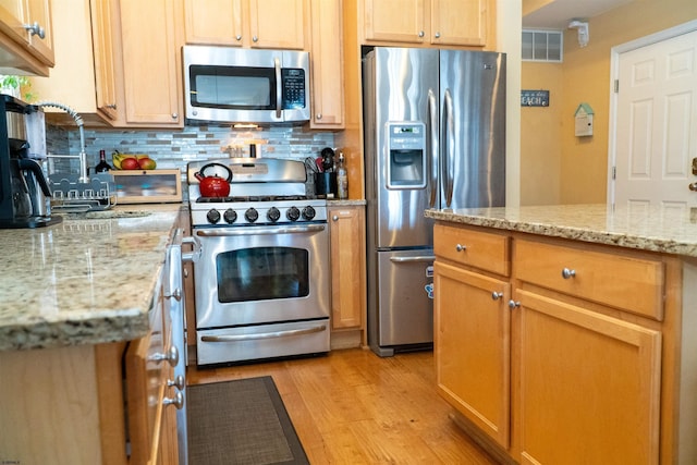 kitchen with visible vents, light wood-style flooring, tasteful backsplash, stainless steel appliances, and light stone countertops