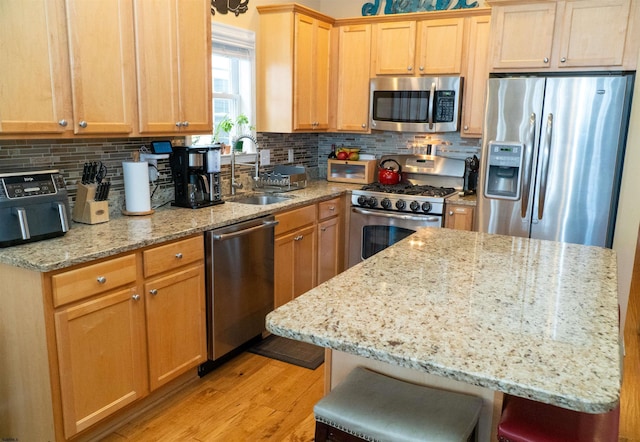 kitchen with light stone counters, light wood finished floors, a sink, decorative backsplash, and stainless steel appliances