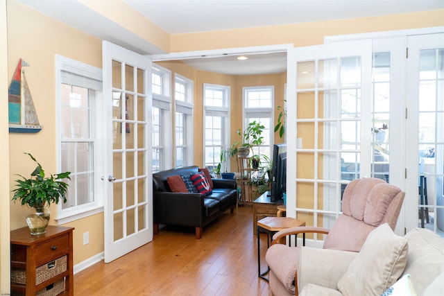 living area with french doors, baseboards, and light wood finished floors