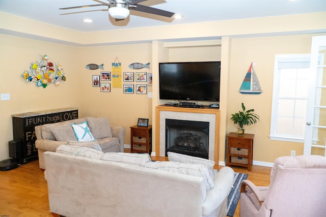 living area featuring a fireplace, baseboards, light wood-type flooring, and a ceiling fan