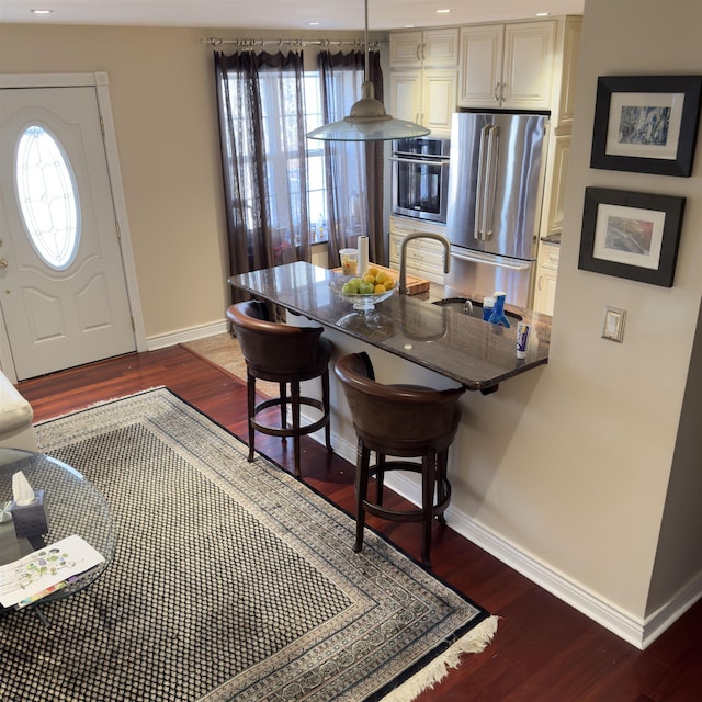 kitchen featuring baseboards, dark stone counters, stainless steel appliances, dark wood-type flooring, and a kitchen bar