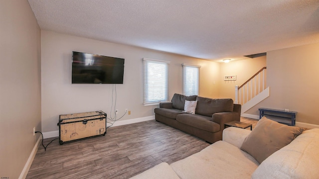 living area featuring stairway, a textured ceiling, baseboards, and wood finished floors