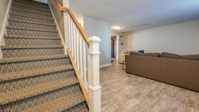 stairs with wood finished floors, baseboards, and a textured ceiling