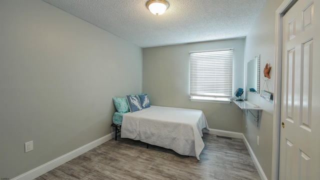 bedroom featuring visible vents, a textured ceiling, baseboards, and wood finished floors