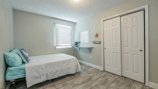 bedroom with a closet, a textured ceiling, baseboards, and wood finished floors