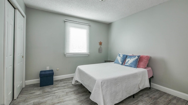 bedroom featuring a closet, a textured ceiling, baseboards, and wood finished floors